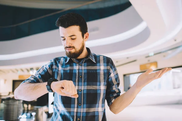 Ernstige man die op zijn horloge terwijl staande op de stedelijke achtergrond — Stockfoto