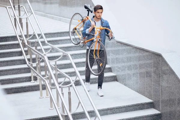 Der Typ in der blauen Jeansjacke, der sein schulterorangefarbenes Fahrrad trägt. — Stockfoto