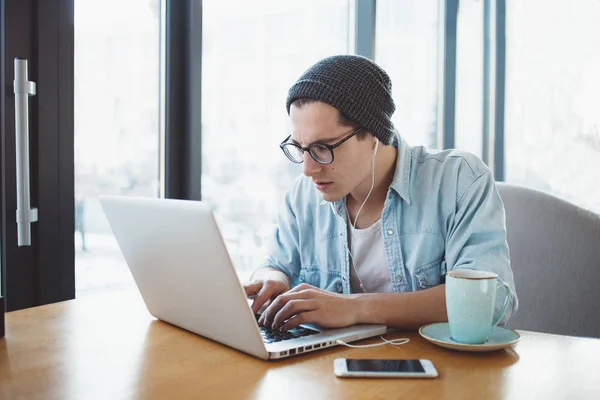 Bonito homem de negócios em desgaste casual e óculos está usando um laptop no café — Fotografia de Stock