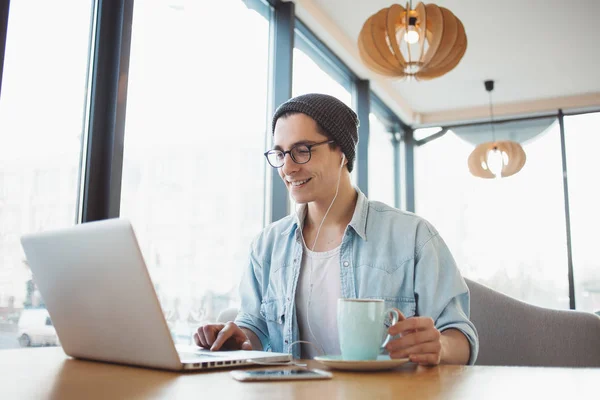 Bonito homem de negócios em desgaste casual e óculos está usando um laptop no café — Fotografia de Stock