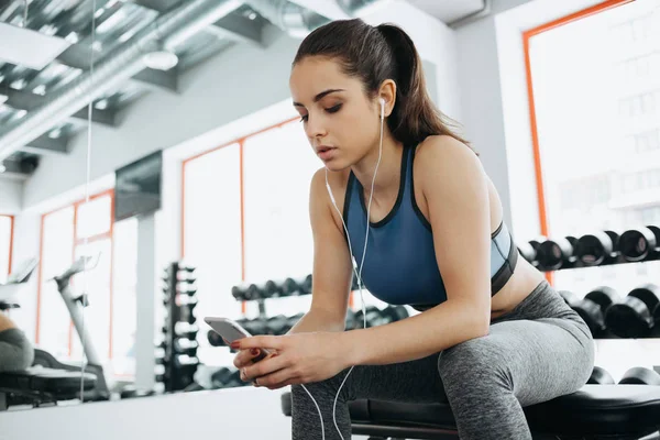 Mujer joven con auriculares escuchando música después de entrenar duro en el gimnasio . — Foto de Stock