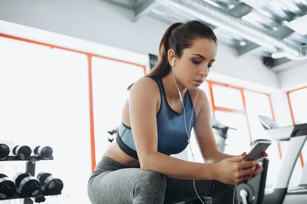 Ung kvinna med hörlurar lyssnar på musik efter hårt träningspass i gymmet. — Stockfoto