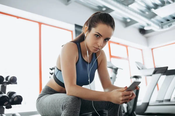 带着耳机听音乐后，硬在健身房锻炼的年轻女人. — 图库照片