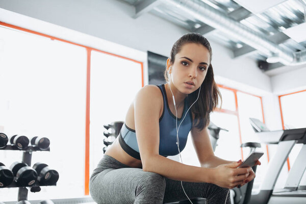 Young woman with earphones listening to music after hard workout in gym.