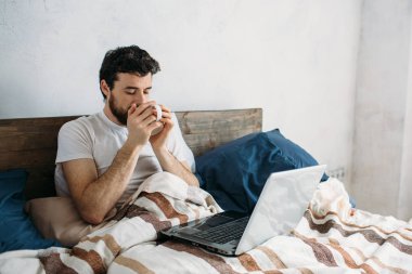 Kahve ya da çay Kupası ile sabah yatakta yatan sakallı adam