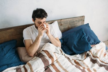 Kahve ya da çay Kupası ile sabah yatakta yatan sakallı adam