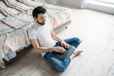 Genç adam yerde yatağın yanında oturarak