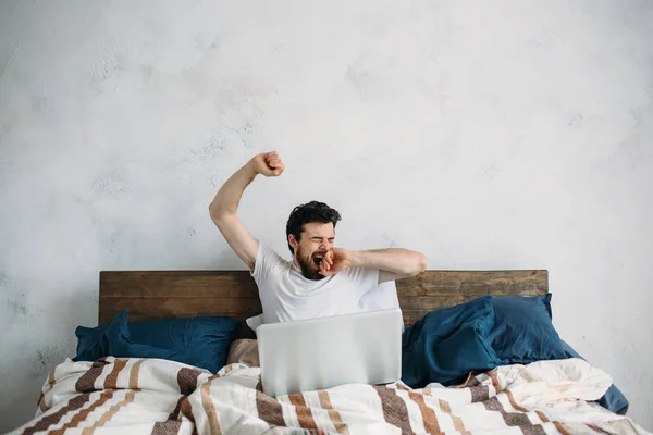 Schöner Mann sitzt im Bett und dehnt sich — Stockfoto