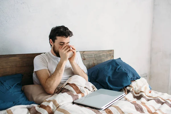 Bärtiger Mann liegt im Morgenbett mit Kaffee- oder Teetasse — Stockfoto