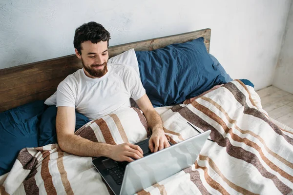 Bärtiger Mann liegt mit Laptop im Morgenbett — Stockfoto