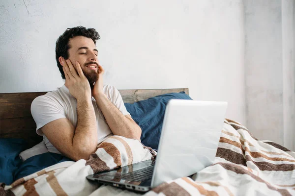 Bebaarde man liggen in ochtend bed met laptop — Stockfoto