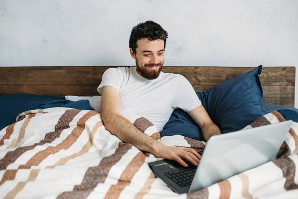 Bärtiger Mann liegt mit Laptop im Morgenbett — Stockfoto