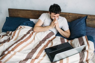 Dizüstü bilgisayar ile sabah yatakta yatan sakallı adam