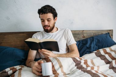 Sakallı adam onun yatak odasında yalan büyük bir kitap okuma.