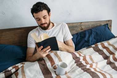 Sakallı adam onun yatak odasında yalan büyük bir kitap okuma.