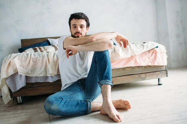 Jonge man zitten op de grond in de buurt van het bed — Stockfoto