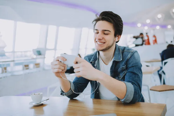 Привлекательный молодой человек или фрилансер сидит в кафе и пользуется своим мобильным телефоном — стоковое фото