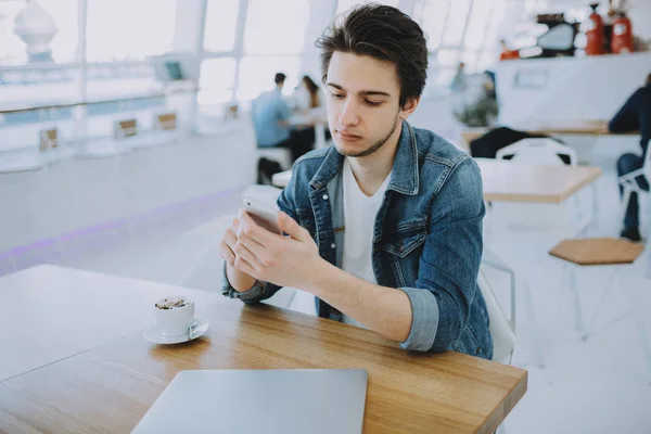 Aantrekkelijke jonge man of freelancer met mobile is zitten in Cafe en koffie drinken — Stockfoto