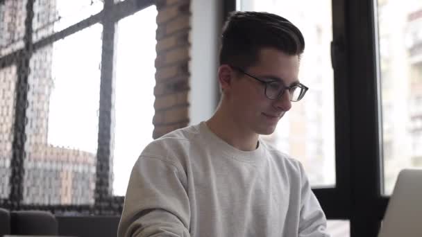 Bonito homem de negócios em desgaste casual e óculos está usando um laptop no café — Vídeo de Stock