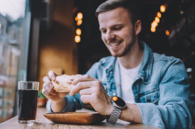 Bir restoranda oturan ve bir hamburger yeme genç adam
