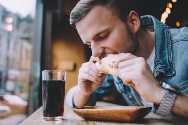 Bir restoranda oturan ve bir hamburger yeme genç adam