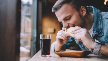 Bir restoranda oturan ve bir hamburger yeme genç adam