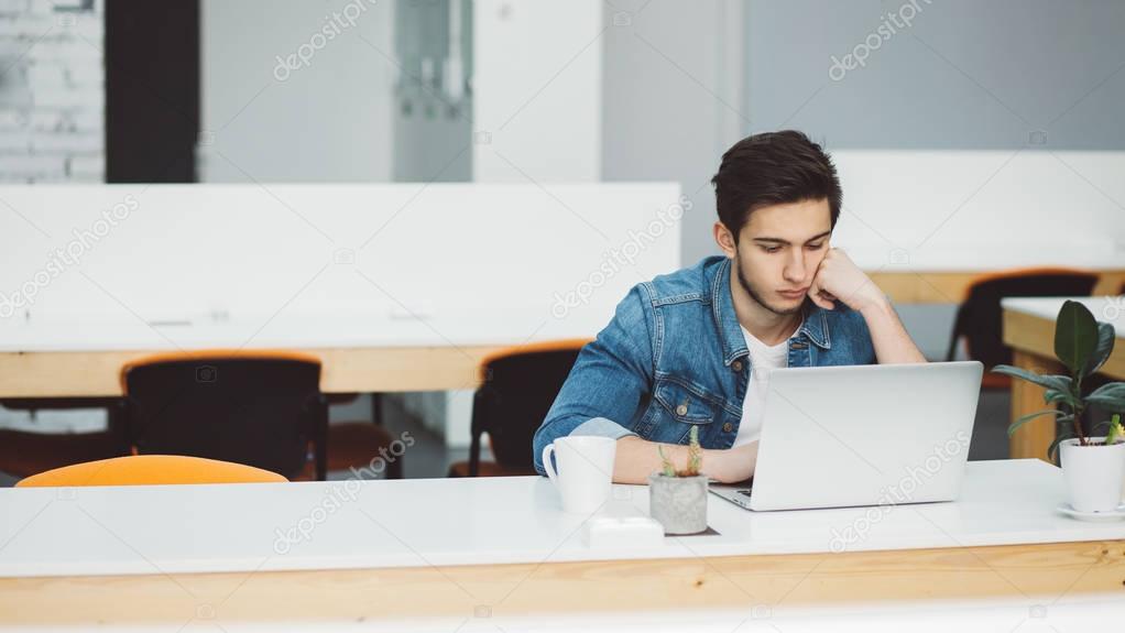 Serious young guy with beard working on laptop
