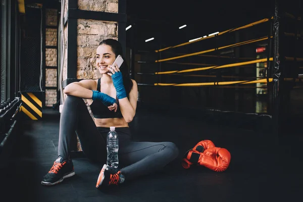 Mujer joven sentada en el suelo después de entrenar duro en el gimnasio . — Foto de Stock