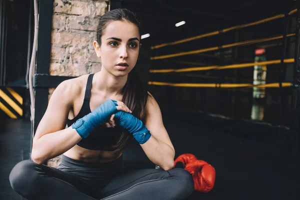 Mujer joven sentada en el suelo después de entrenar duro en el gimnasio . — Foto de Stock