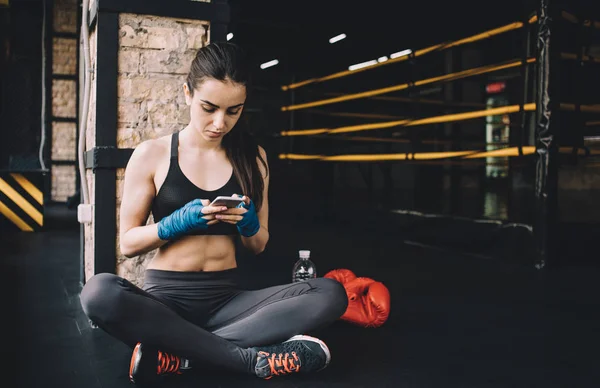 Mujer joven sentada en el suelo después de entrenar duro en el gimnasio . — Foto de Stock