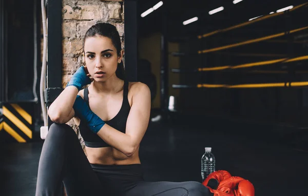 Jonge vrouw zittend op de vloer na zware training in de sportschool. — Stockfoto