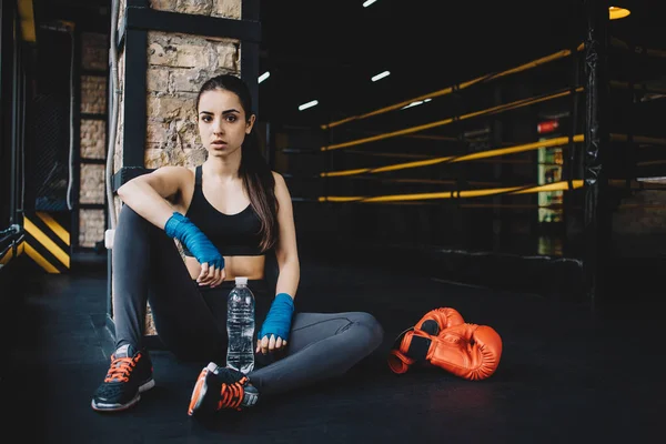 Jonge vrouw zittend op de vloer na zware training in de sportschool. — Stockfoto