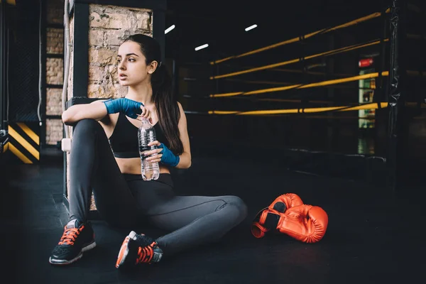 Jonge vrouw zittend op de vloer na zware training in de sportschool. — Stockfoto