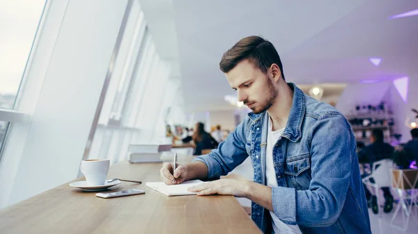 Le gars est assis devant la table près de la fenêtre — Photo