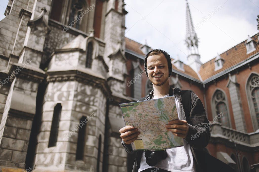 The picture of a traveller that is standing near the church. He is holding the map in his hands