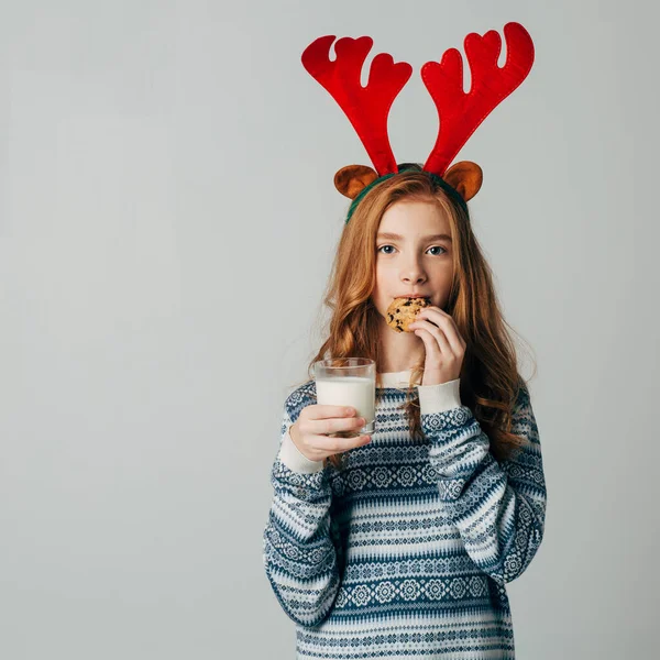 Chica pelirroja con cuernos rojos en un suéter es muy aficionado a la leche con galletas por noche. Ella no esperó a Santa y se comió su regalo. El adolescente en Navidad antes del nuevo año — Foto de Stock