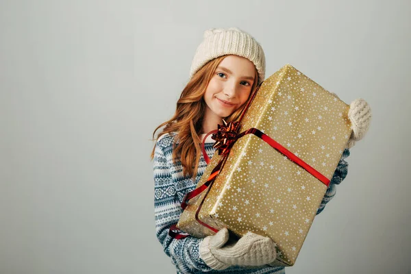 Adolescente en un sombrero de punto, suéter y guantes. Una chica abraza su regalo de Navidad de sus padres. Sus amigos agradablemente sorprendieron el Año Nuevo . Fotos De Stock Sin Royalties Gratis