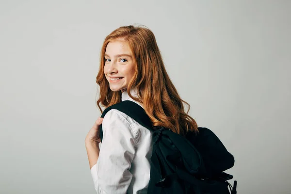 Una joven pelirroja va a la escuela. Colegiala mirando por encima de su hombro y va a estudiar lecciones. Aislar sobre fondo blanco Fotos De Stock Sin Royalties Gratis