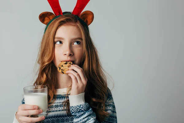Chica pelirroja con cuernos rojos en un suéter es muy aficionado a la leche con galletas por noche. Ella no esperó a Santa y se comió su regalo. El adolescente en Navidad antes del nuevo año Imagen De Stock