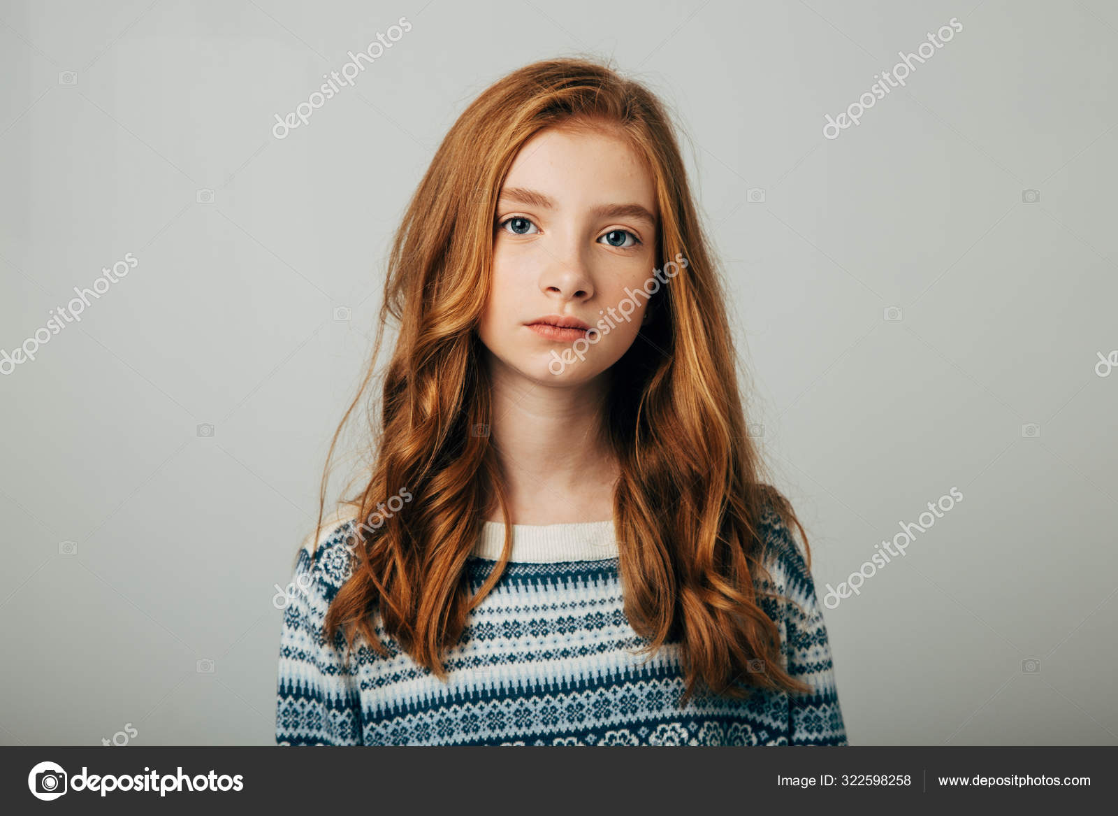A young red-haired girl in a blue sweater looks at the camera. A girl with