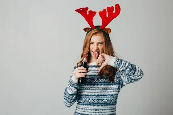 Chica pelirroja rechaza la soda en Navidad para no dañar el azúcar con su salud. adolescente con cuernos de ciervo rojo antes del año nuevo. Ella no aprueba las bebidas saharauis. Construye una mueca de asco Imagen De Stock