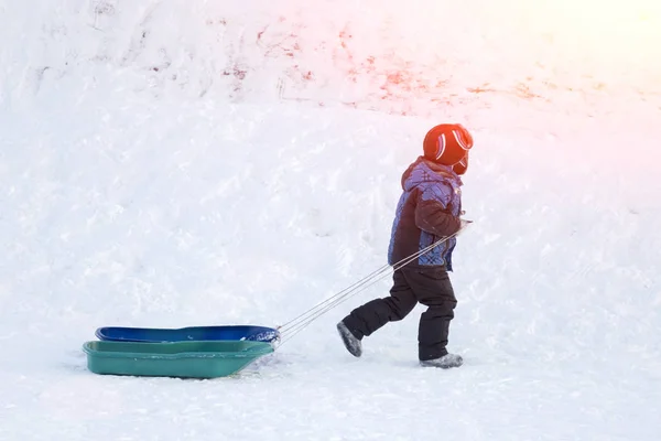 Bambino con una slitta nella neve nella giornata di sole Immagini Stock Royalty Free