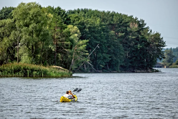 Kayaking. Couple paddling on yellow inflated kayak on  the lake or river with green forest on the bank