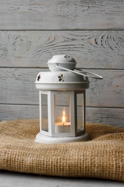 Kahverengi masa örtüsü içinde yanan bir mum ile beyaz fener. Dekoratif yıldız şamdan. Ahşap arka plan. Mumlar yanında gümüş hediye kutusu.