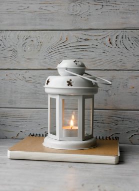 Kahverengi masa örtüsü içinde yanan bir mum ile beyaz fener. Dekoratif yıldız şamdan. Ahşap arka plan. Mumlar yanında gümüş hediye kutusu.