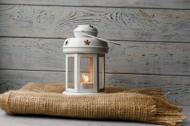 Kahverengi masa örtüsü içinde yanan bir mum ile beyaz fener. Dekoratif yıldız şamdan. Ahşap arka plan. Mumlar yanında gümüş hediye kutusu.