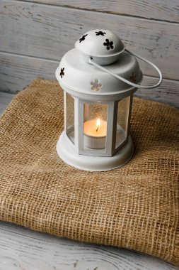 Kahverengi masa örtüsü içinde yanan bir mum ile beyaz fener. Dekoratif yıldız şamdan. Ahşap arka plan. Mumlar yanında gümüş hediye kutusu.