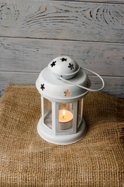 Kahverengi masa örtüsü içinde yanan bir mum ile beyaz fener. Dekoratif yıldız şamdan. Ahşap arka plan. Mumlar yanında gümüş hediye kutusu.