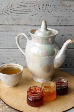 Ahşap tepsi üzerinde ev yapımı Berry üç küçük kavanoz reçel. Sağlıklı gıda fikirler. Çaydanlık ve yeşil çay bir arka plan üzerinde çay fincanı. Gül ahşap bir masa bir gümüş kaşık yanında bastırdı