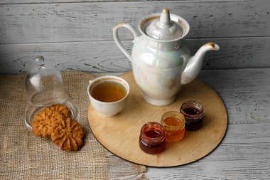 Ahşap tepsi üzerinde ev yapımı Berry üç küçük kavanoz reçel. Sağlıklı gıda fikirler. Çaydanlık ve yeşil çay bir arka plan üzerinde çay fincanı. Gül ahşap bir masa bir gümüş kaşık yanında bastırdı